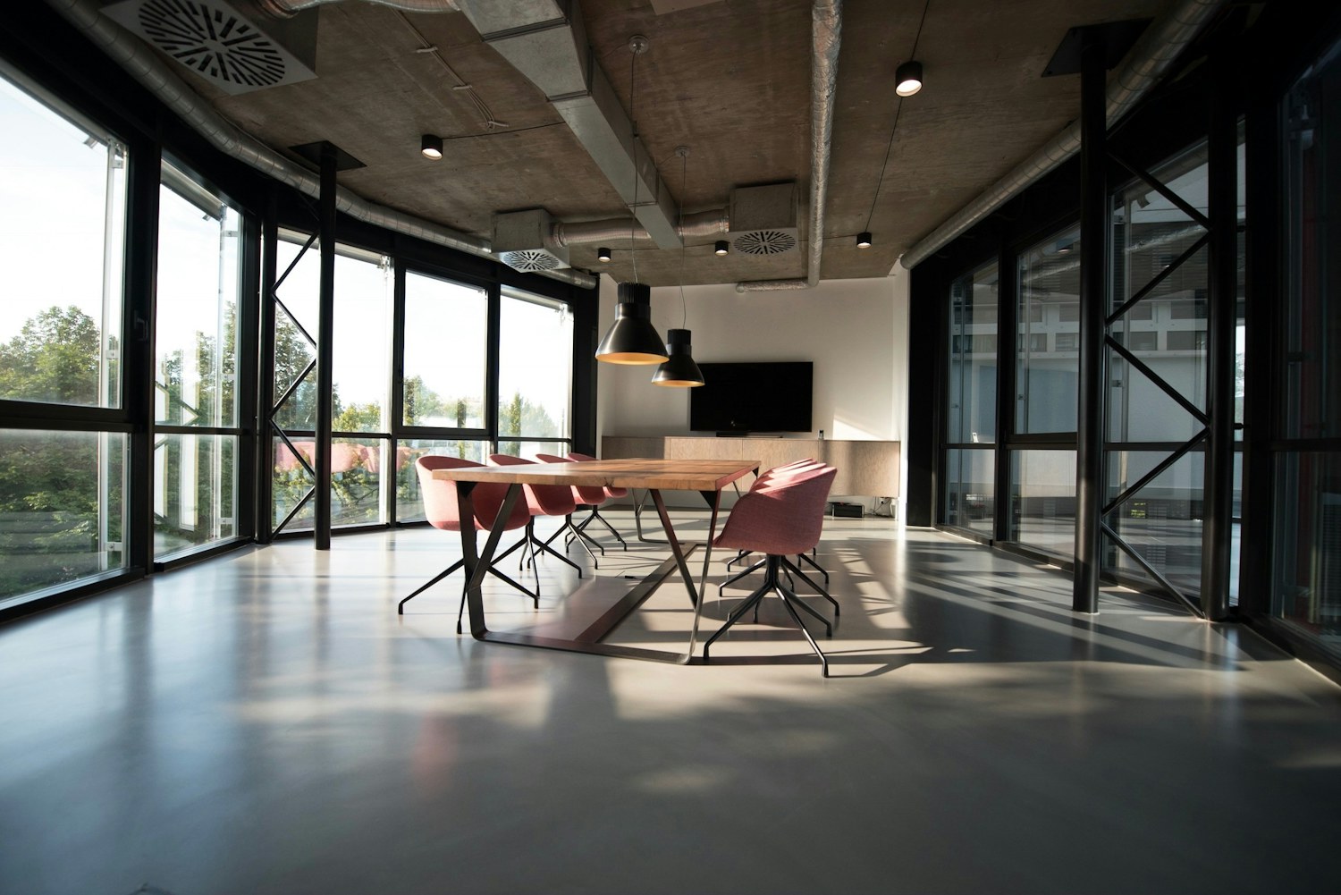 Contemporary office meeting area with glazed walls, a timber table, and pendant lighting.